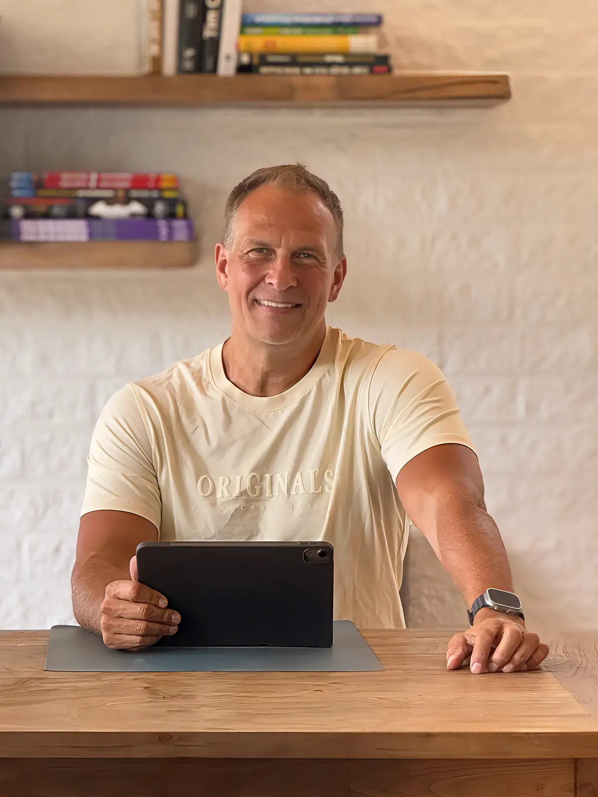 Portrait of Achim Loobes, the solo developer of VigiGym, leaning on a wooden desk with an iPad and smiling at the camera