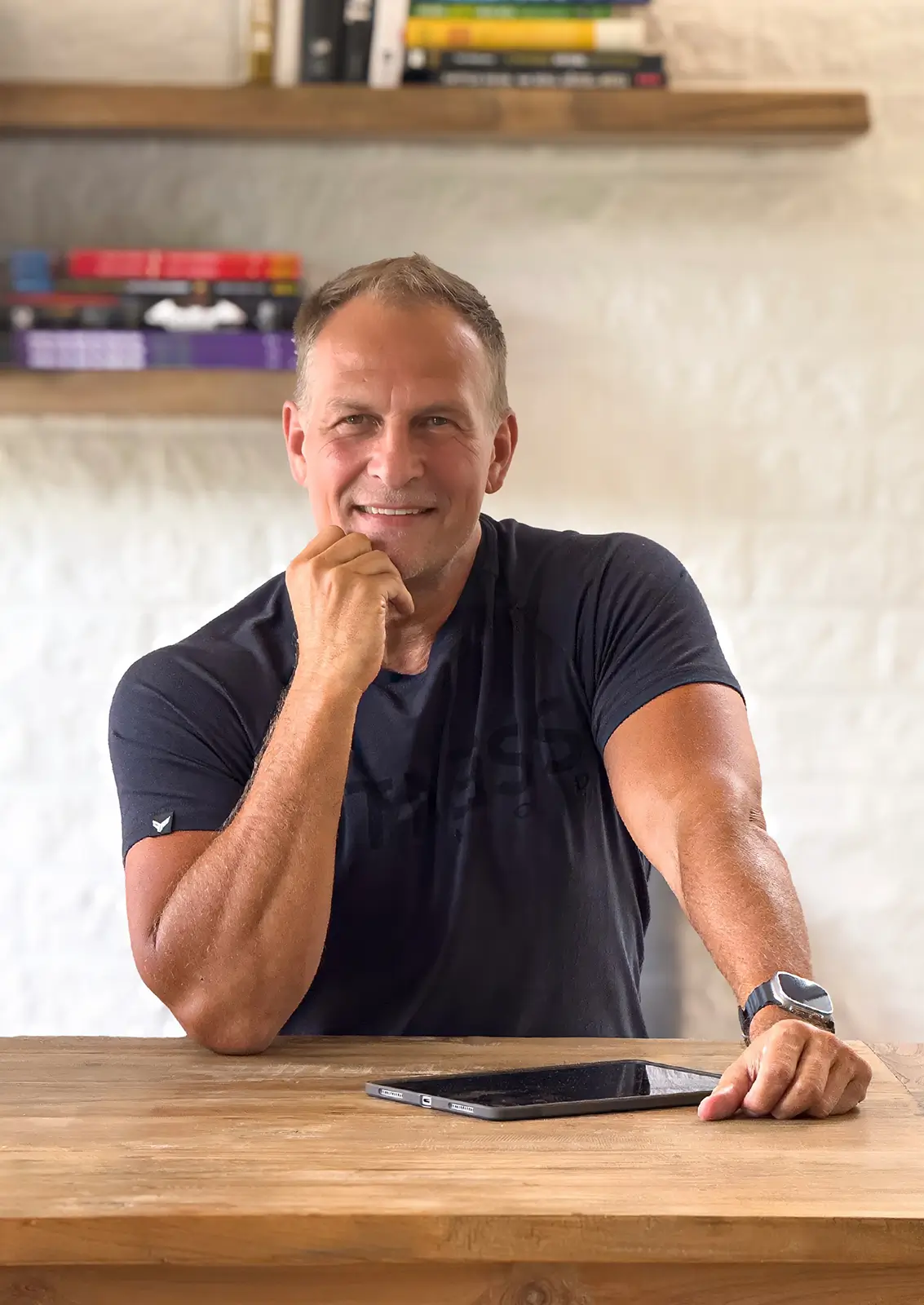 Portrait of Achim Loobes, the solo developer of VigiGym, leaning on a wooden desk with an iPad and smiling at the camera